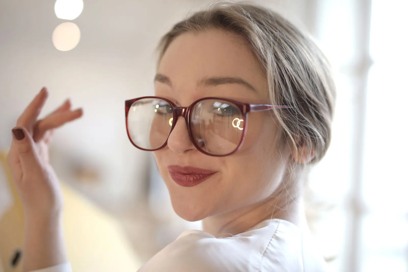 Close-up of a happy woman wearing large eyeglasses, smiling in a bright indoor setting.
